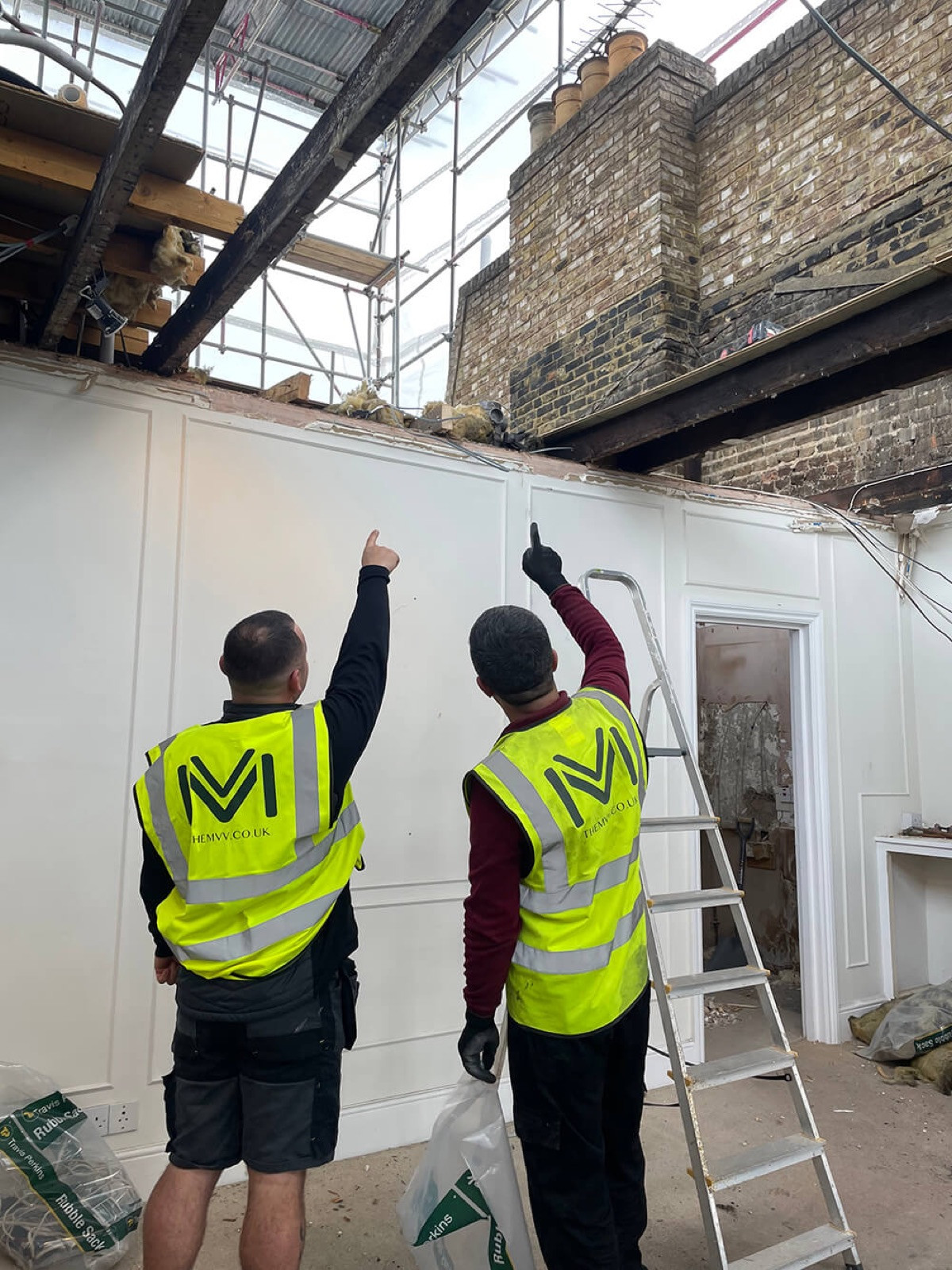 Two MVV site team members point up at an opened roof, with scaffolding and a temporary roof overhead, during a loft extension at Ladbroke Grove.