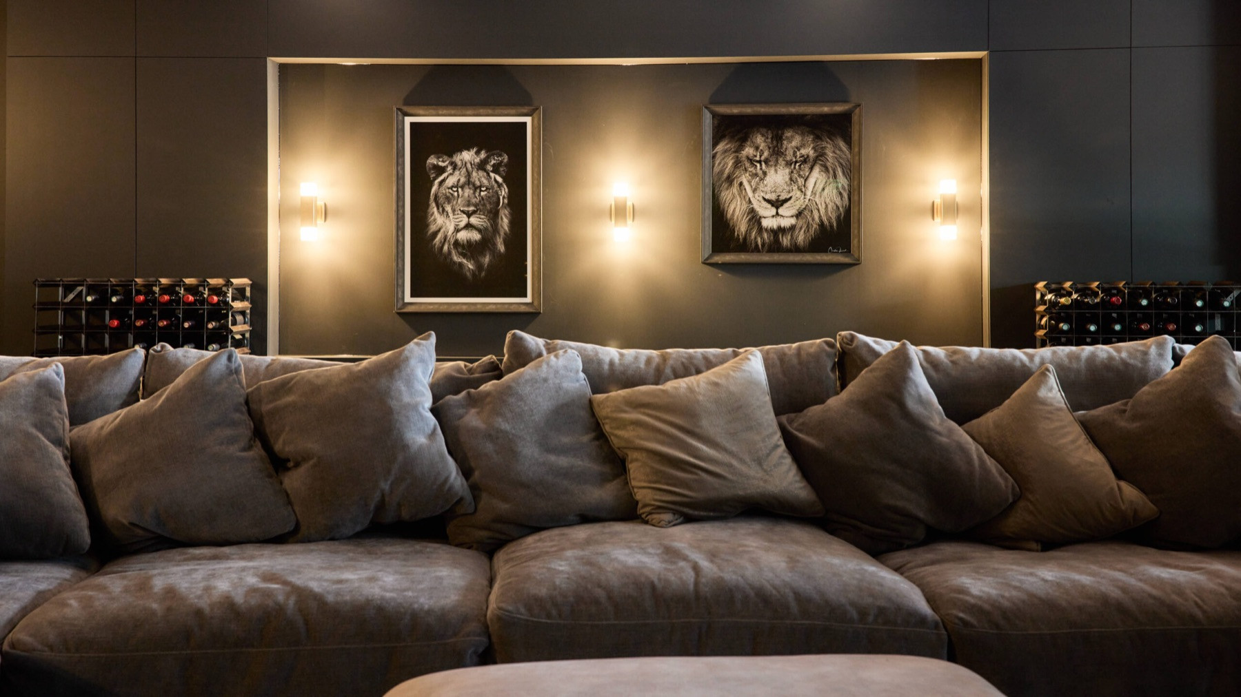 Three wall lights, one either side of two framed lion prints and one between them, above a deep grey sofa at Ellerby Street, Fulham.