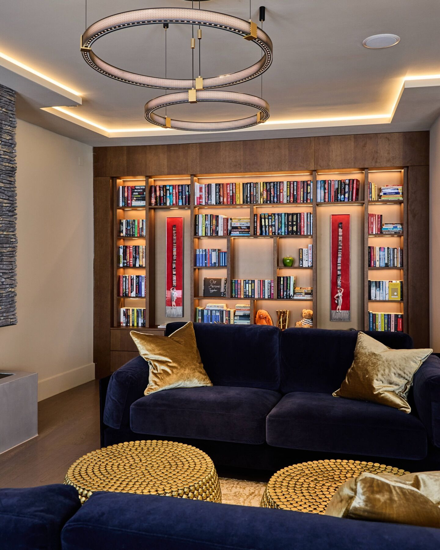 Living room at Ellerby Street, Fulham: bookshelves lit from within, a two ring pendant and concealed light around a recessed ceiling, above deep blue velvet sofas.