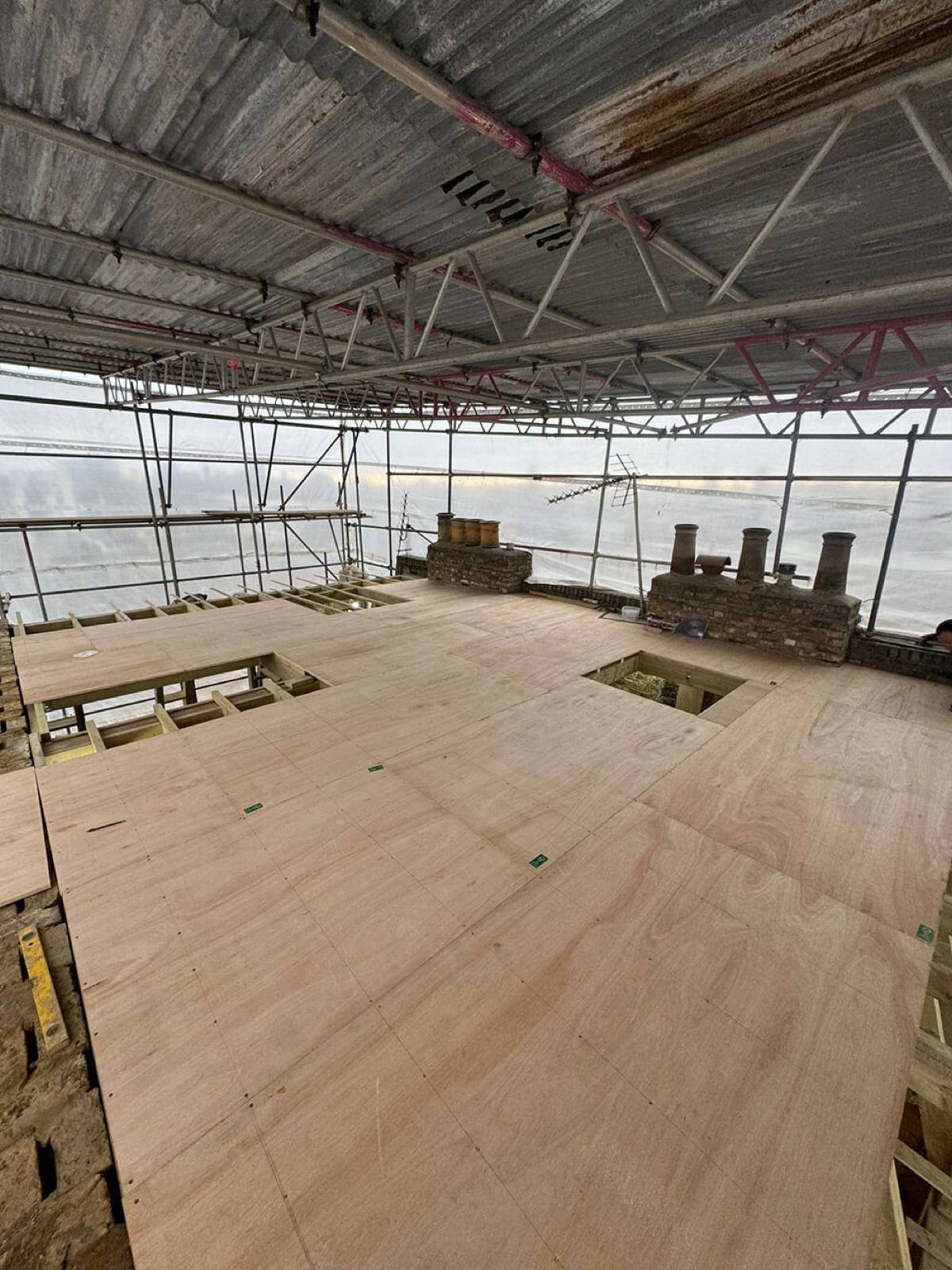 New floor deck and chimney stacks under a temporary scaffold roof during a loft extension adding a storey at Ladbroke Grove, Notting Hill, London, by MVV