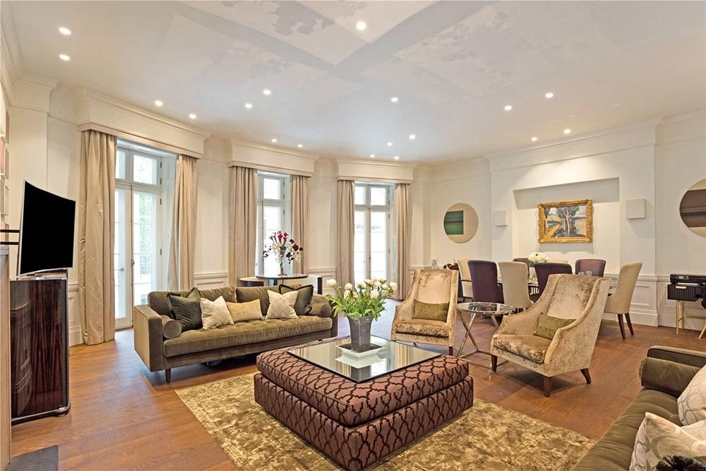 The living and dining room of a two-storey apartment on Park Lane, Mayfair, with tall windows, panelled walls and its original wood flooring restored.