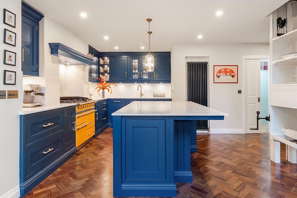 The kitchen at St Germans Place, Blackheath: deep blue cabinetry and island, a yellow range cooker, brass handles and reclaimed herringbone flooring.