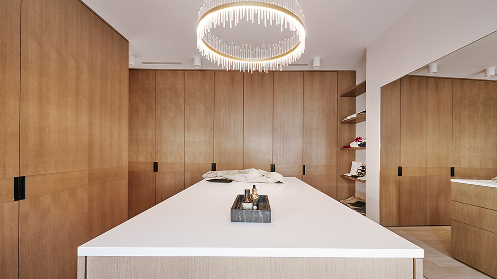 Dressing room with timber joinery, a central island and a ring chandelier at Woodside in Wimbledon, London, designed and built by MVV