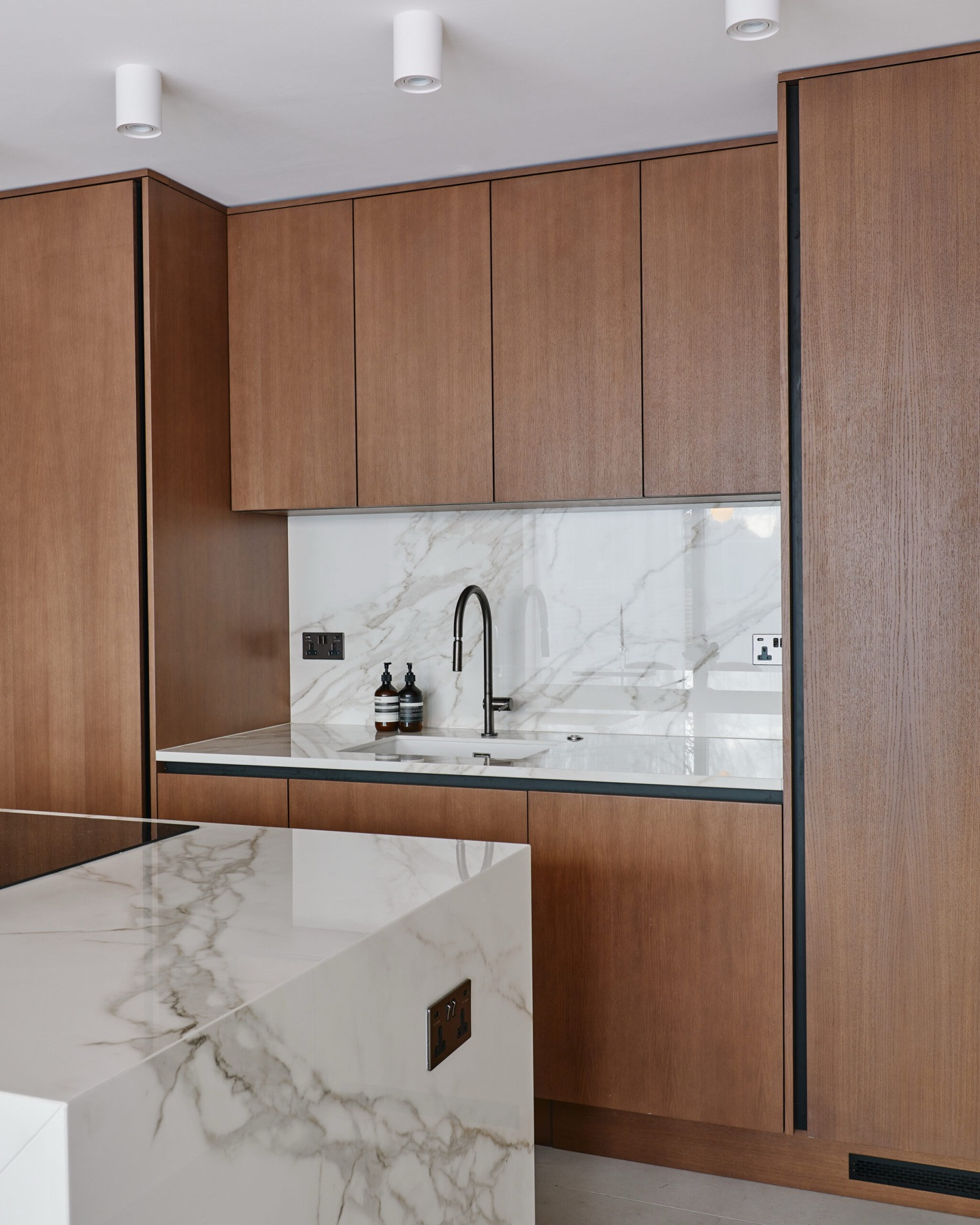 The kitchen at Woodside, Wimbledon: floor to ceiling timber cabinetry, a marble-effect splashback with a black tap, and a marble-effect island in the foreground.